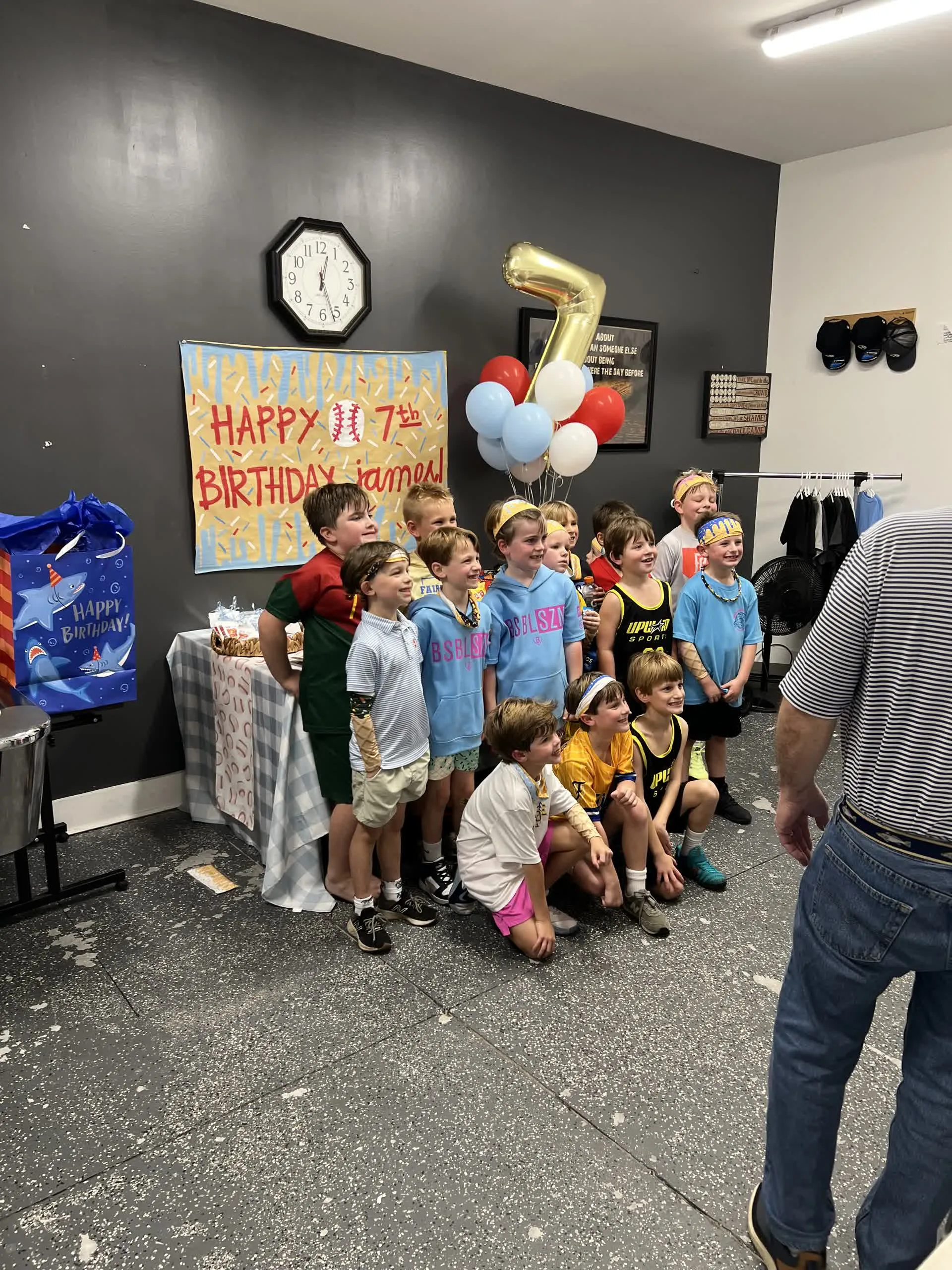 Kids group photo in front of a 'Happy 7th Birthday James' banner with balloons