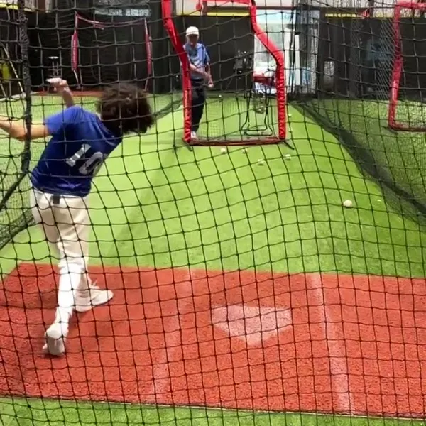 Teen athlete in batting cage with coach observing