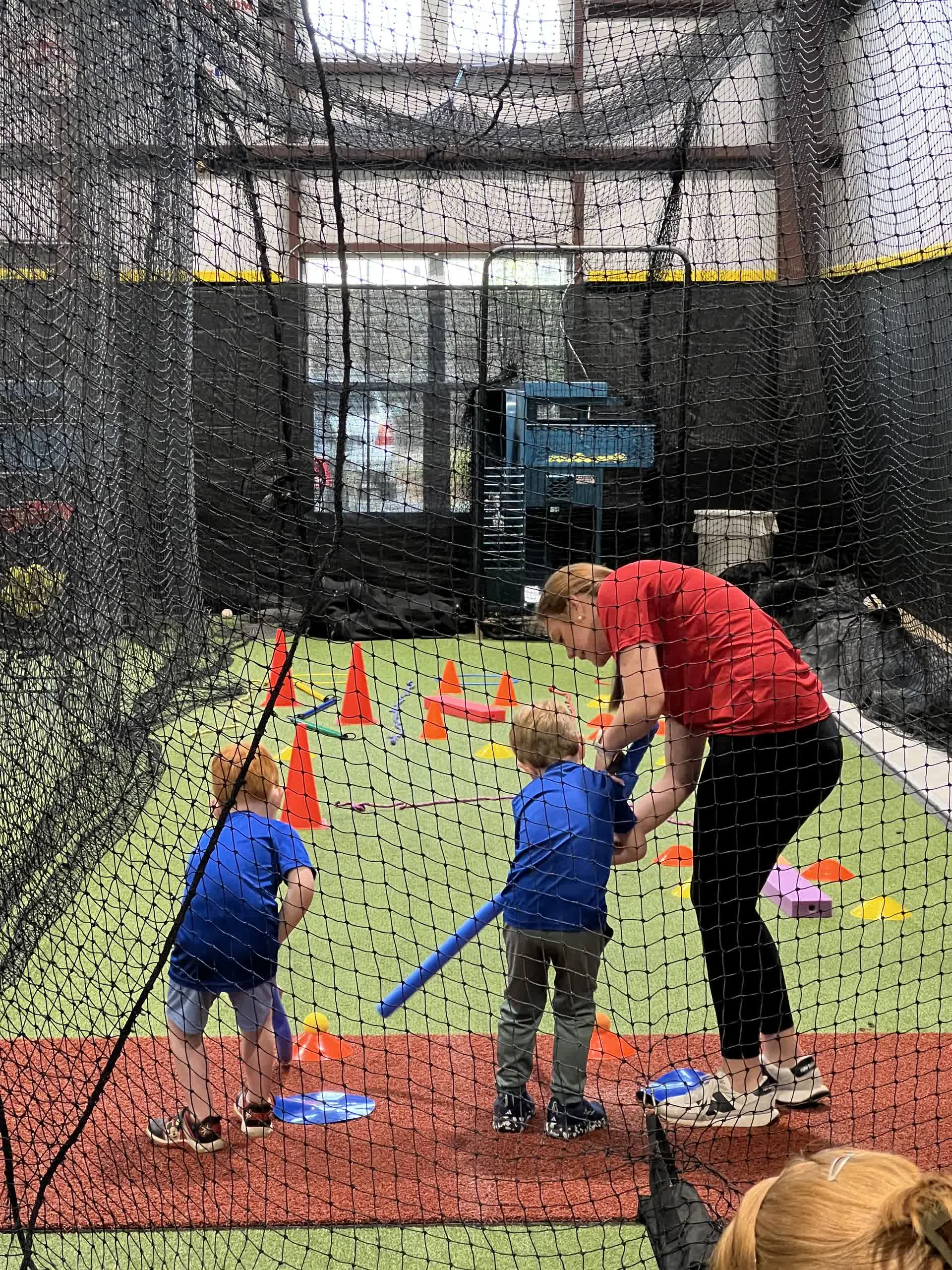 Toddlers with a coach running soccer drills inside the batting cage
